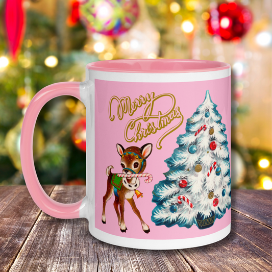 This pink lined ceramic glossy mug features a retro Mid Century 1950s print of a reindeer with candy cane next to a white christmas tree. It features gold lettering that says Merry Christmas.