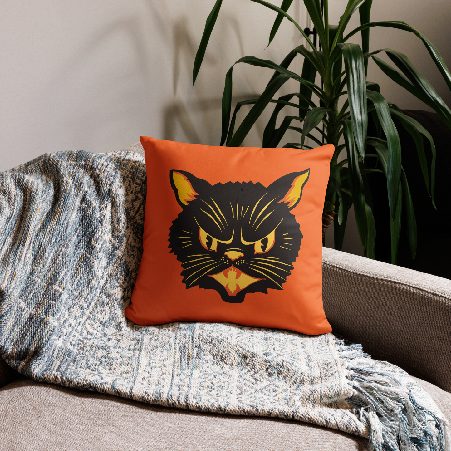 This orange square pillow features a retro Halloween illustration of a black cat with orange and yellow ears, eyes, nose and mouth.