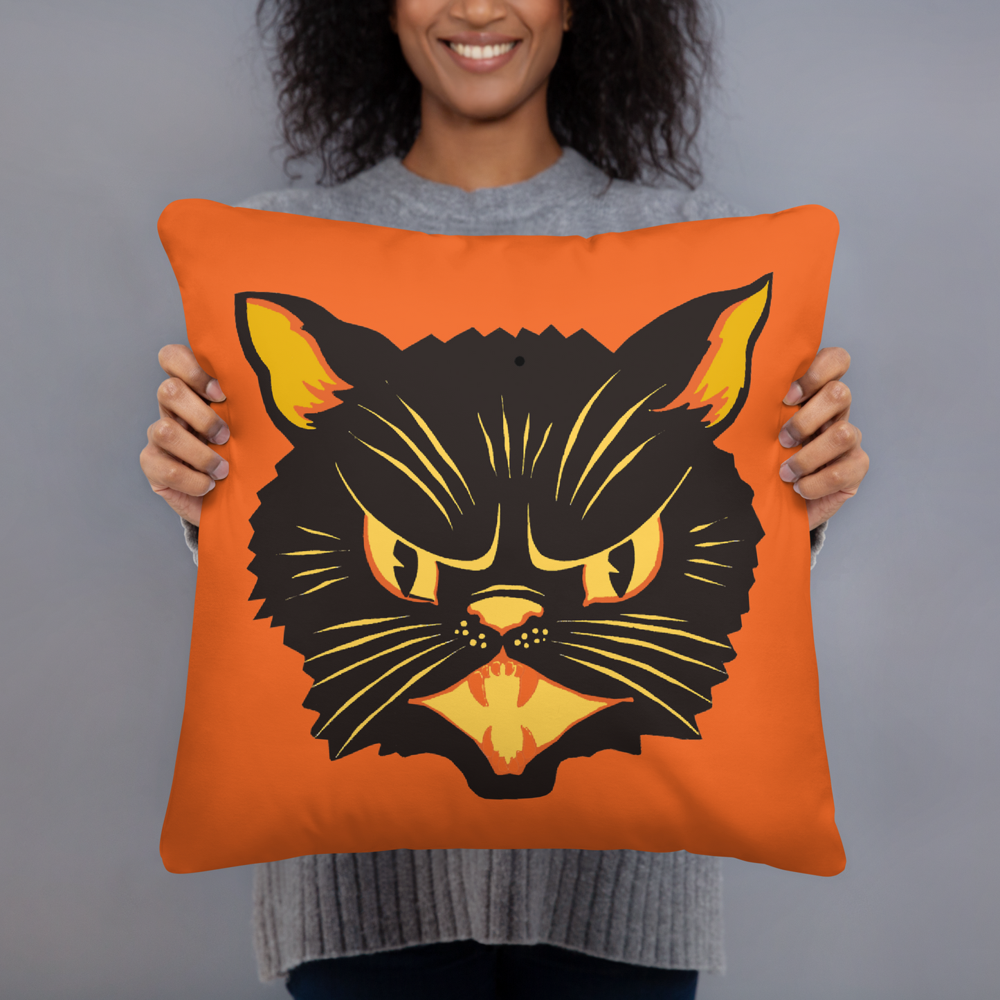 This orange square pillow features a retro Halloween illustration of a black cat with orange and yellow ears, eyes, nose and mouth.