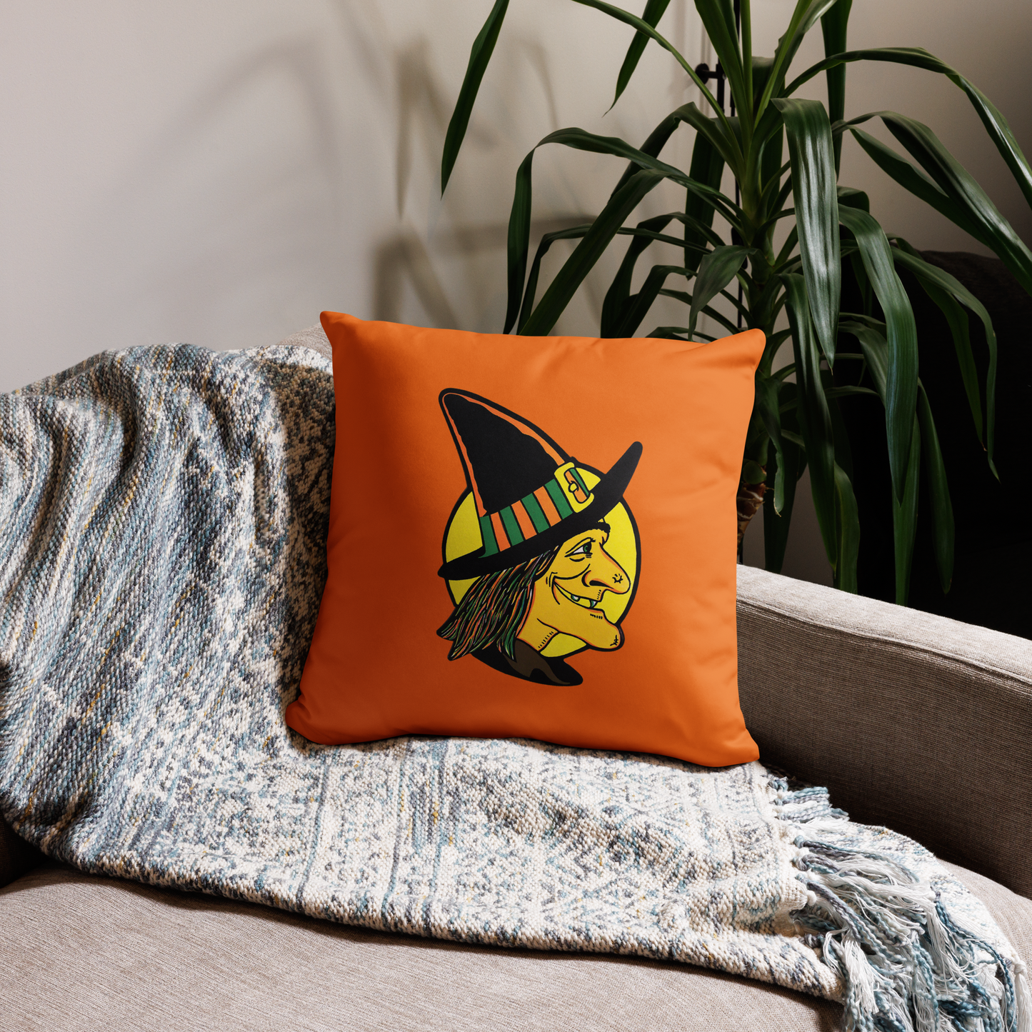 This orange square pillow features a retro Halloween illustration of a witch wearing her pointy hat with a yellow full moon behind her profile.