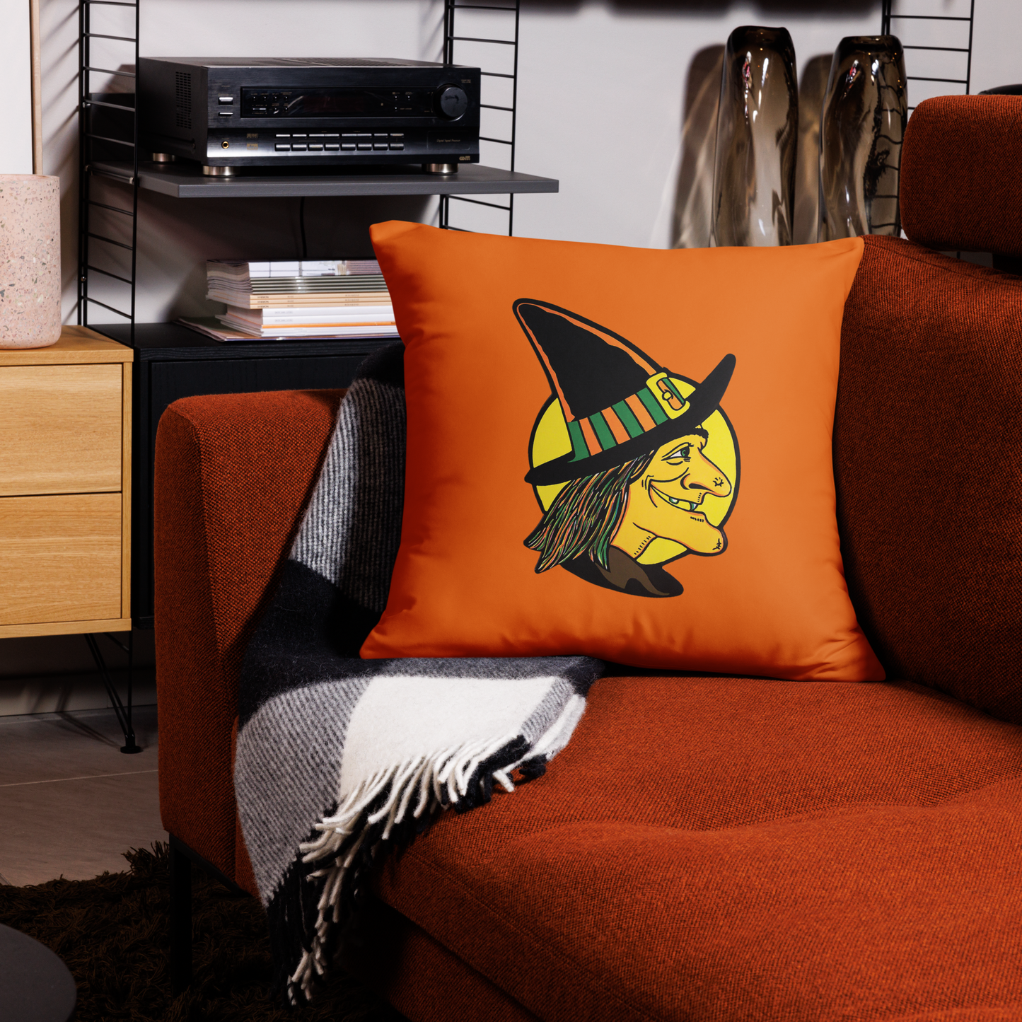 This orange square pillow features a retro Halloween illustration of a witch wearing her pointy hat with a yellow full moon behind her profile.