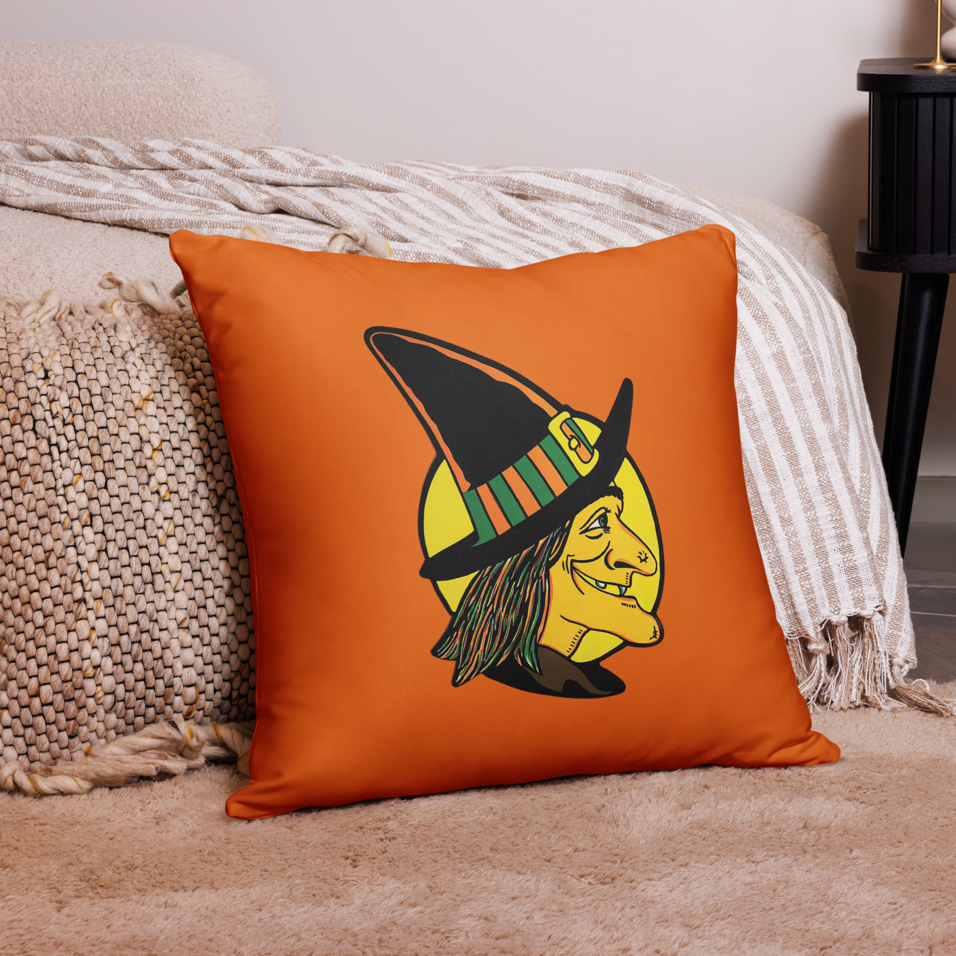 This orange square pillow features a retro Halloween illustration of a witch wearing her pointy hat with a yellow full moon behind her profile.