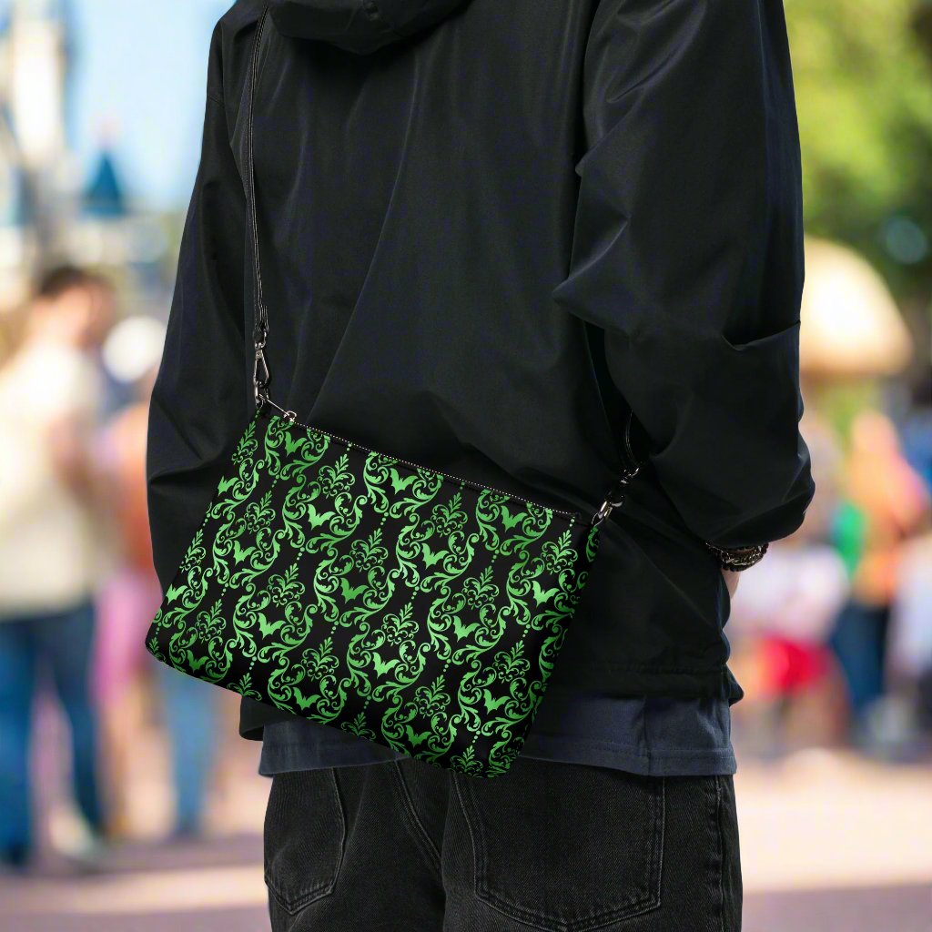 This black crossbody shoulder bag converts into a large wristlet clutch features a retro wallpaper print of green bats and swirls.