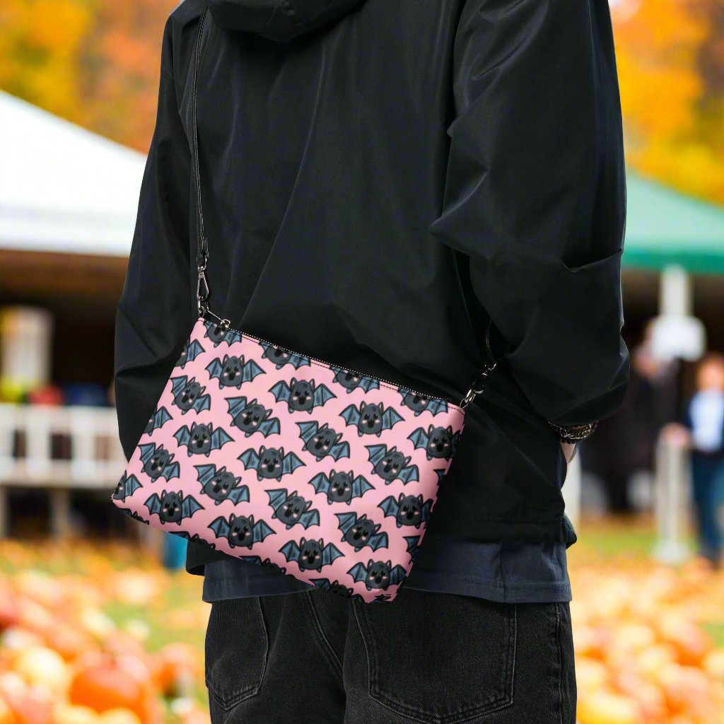 This crossbody shoulder purse converts into a large wristlet clutch. It features adorable grey bats with a pink background.