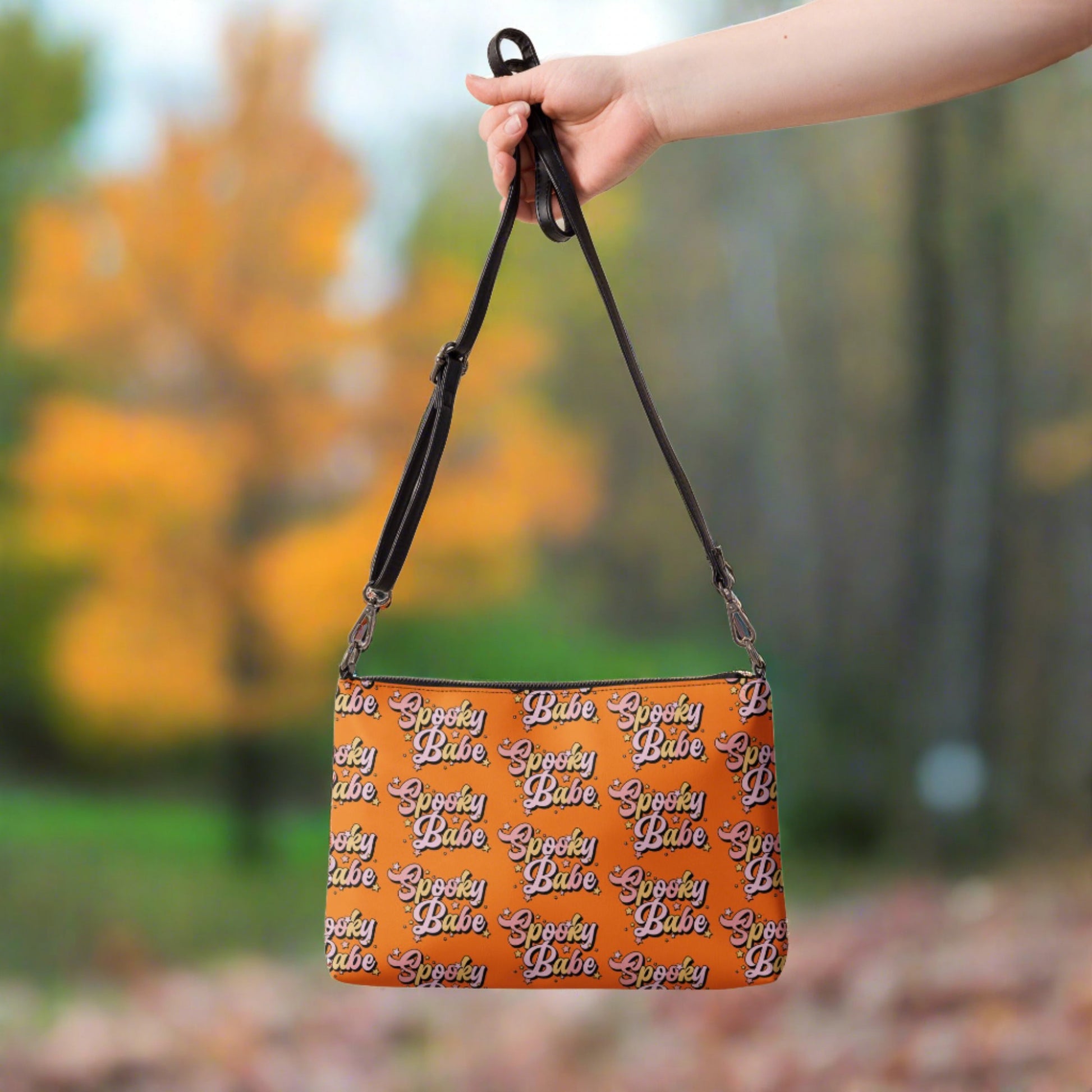 This orange crossbody purse features a retro Barbie style type of lettering that says Spooky Babe in fall pastel colors with stars.