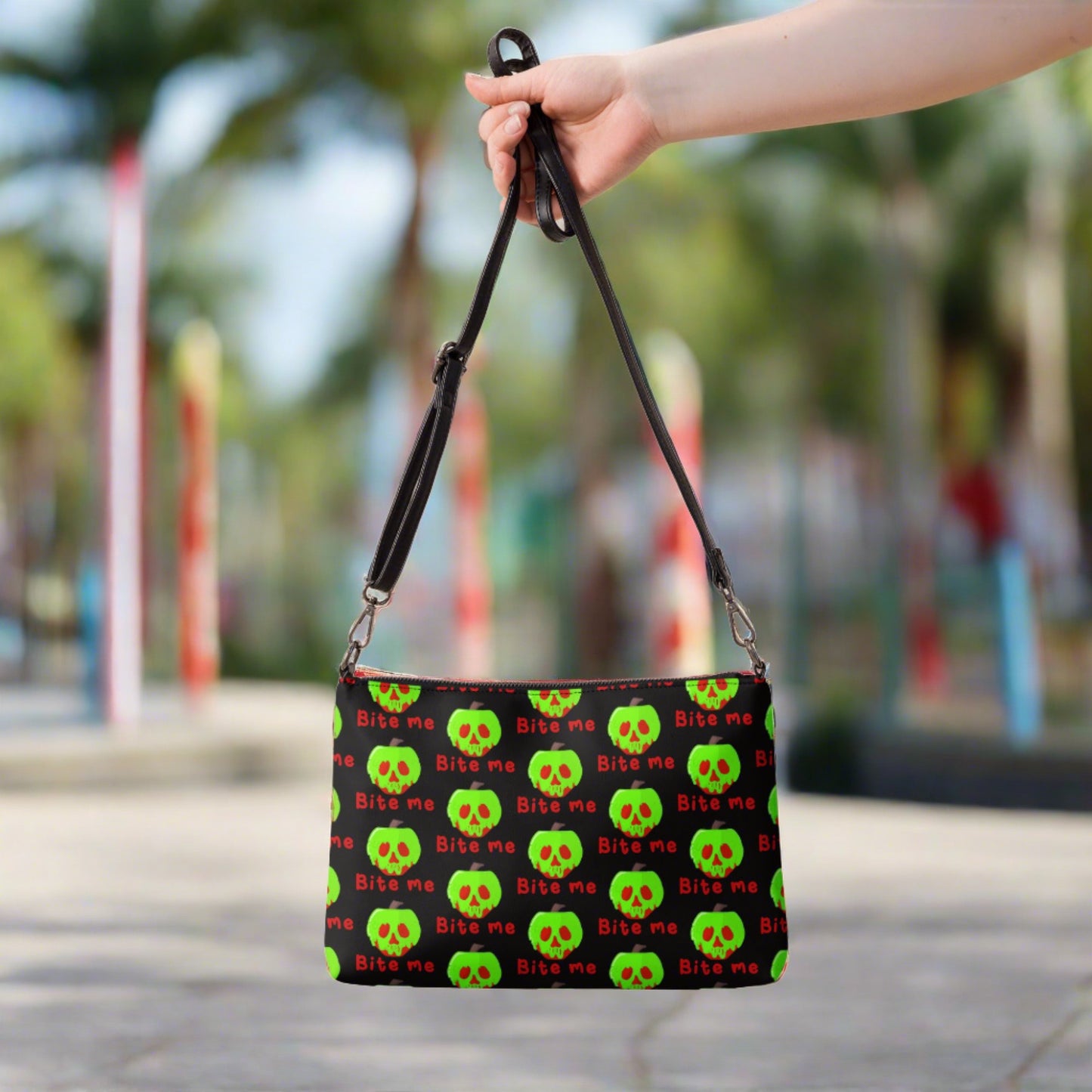 This black crossbody purse features a large red apple dipped in green poison with the words Bite Me underneath and the back is a small size in a patterned print.