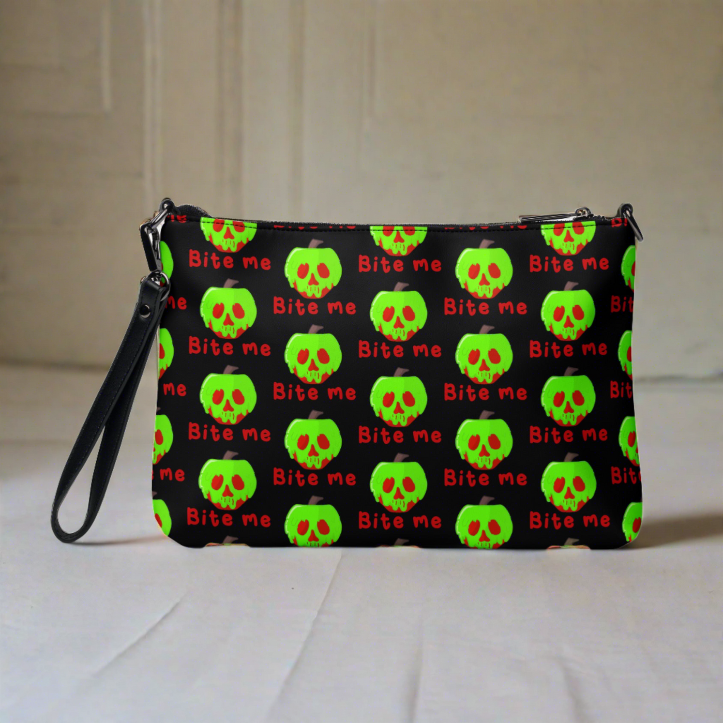 This black crossbody purse features a large red apple dipped in green poison with the words Bite Me underneath and the back is a small size in a patterned print.