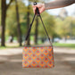 This orange crossbody purse converts to a large wristlet clutch. It features a distressed print of skeleton hands forming a heart with a red heart inside. One side the design is large and the other is a smaller patterned print.