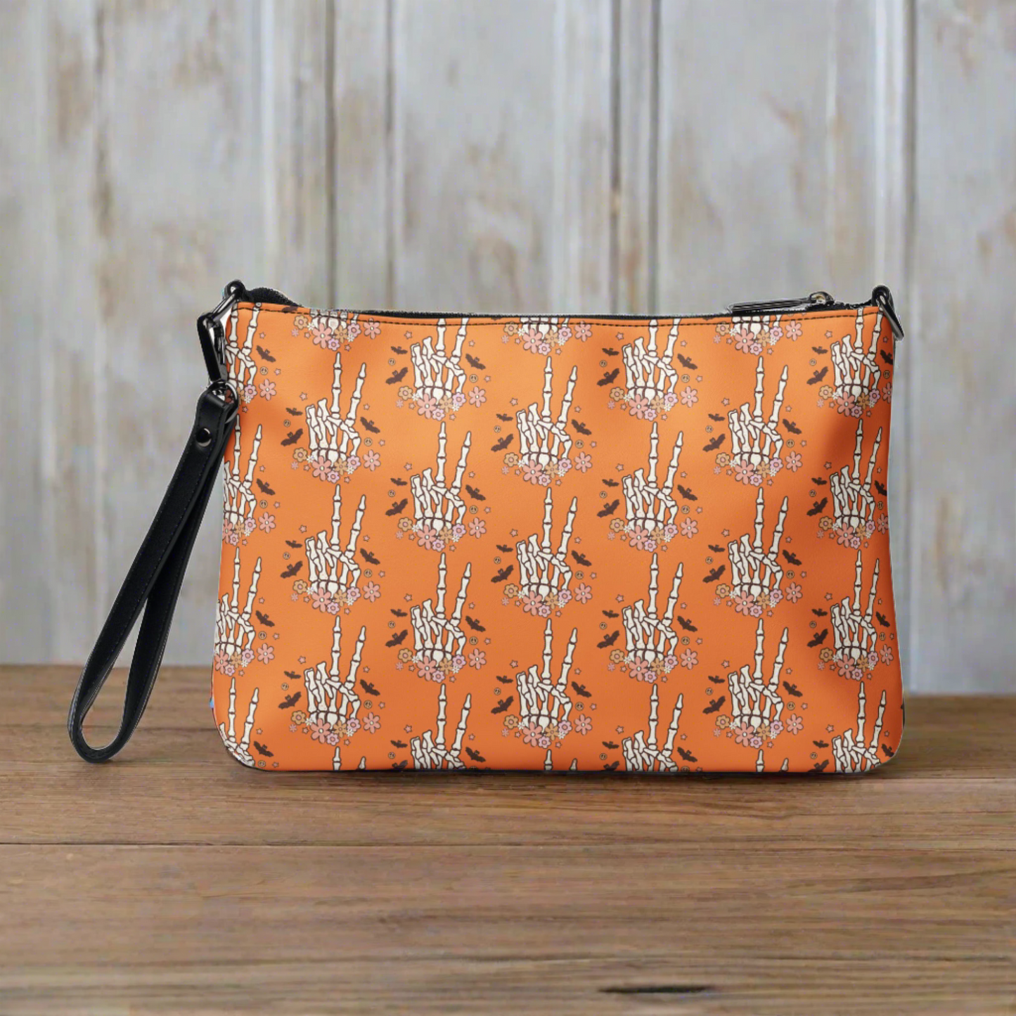 This orange crossbody purse features a skeleton hand making a peace sign surrounded by bats, flowers and peace signs.