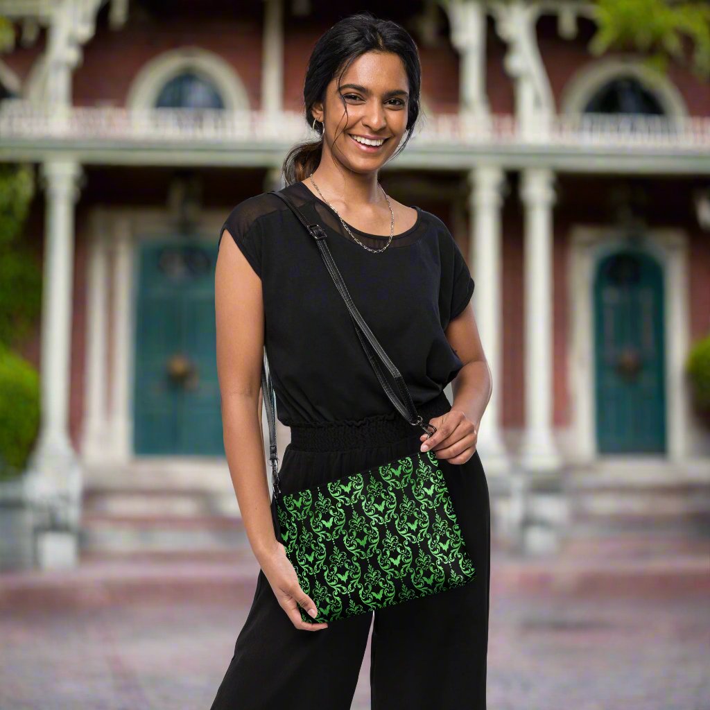 This black crossbody shoulder bag converts into a large wristlet clutch features a retro wallpaper print of green bats and swirls.