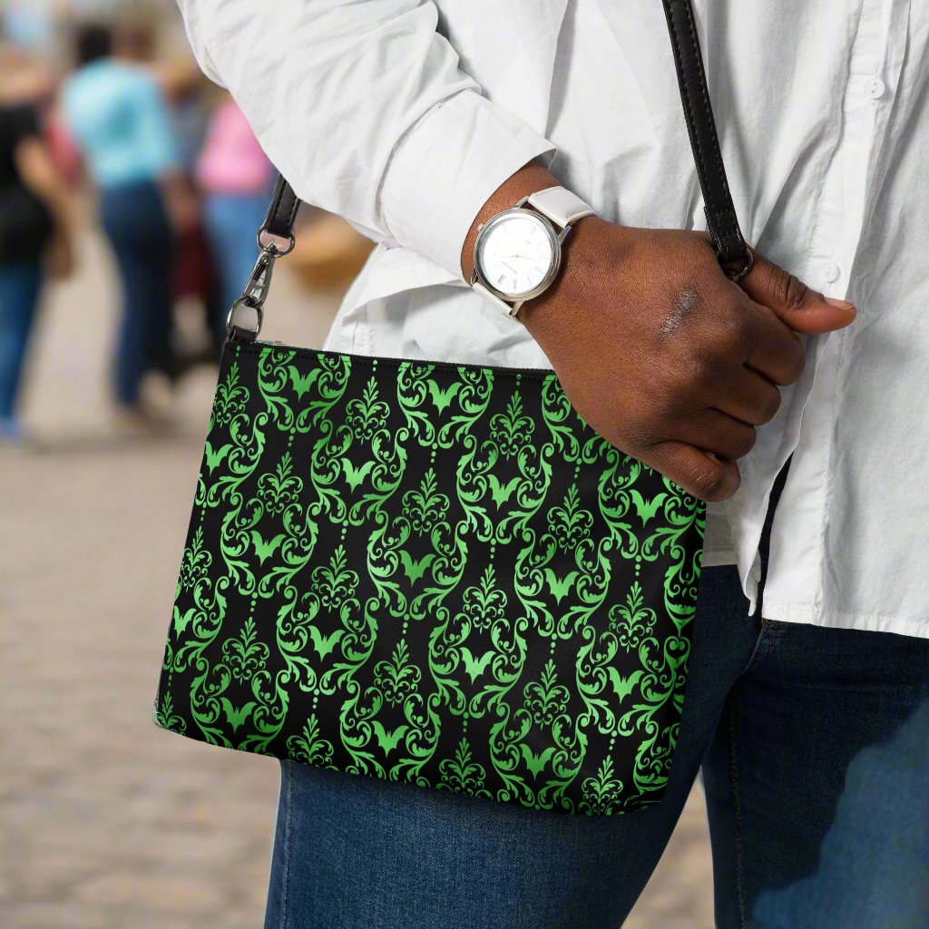 This black crossbody shoulder bag converts into a large wristlet clutch features a retro wallpaper print of green bats and swirls.