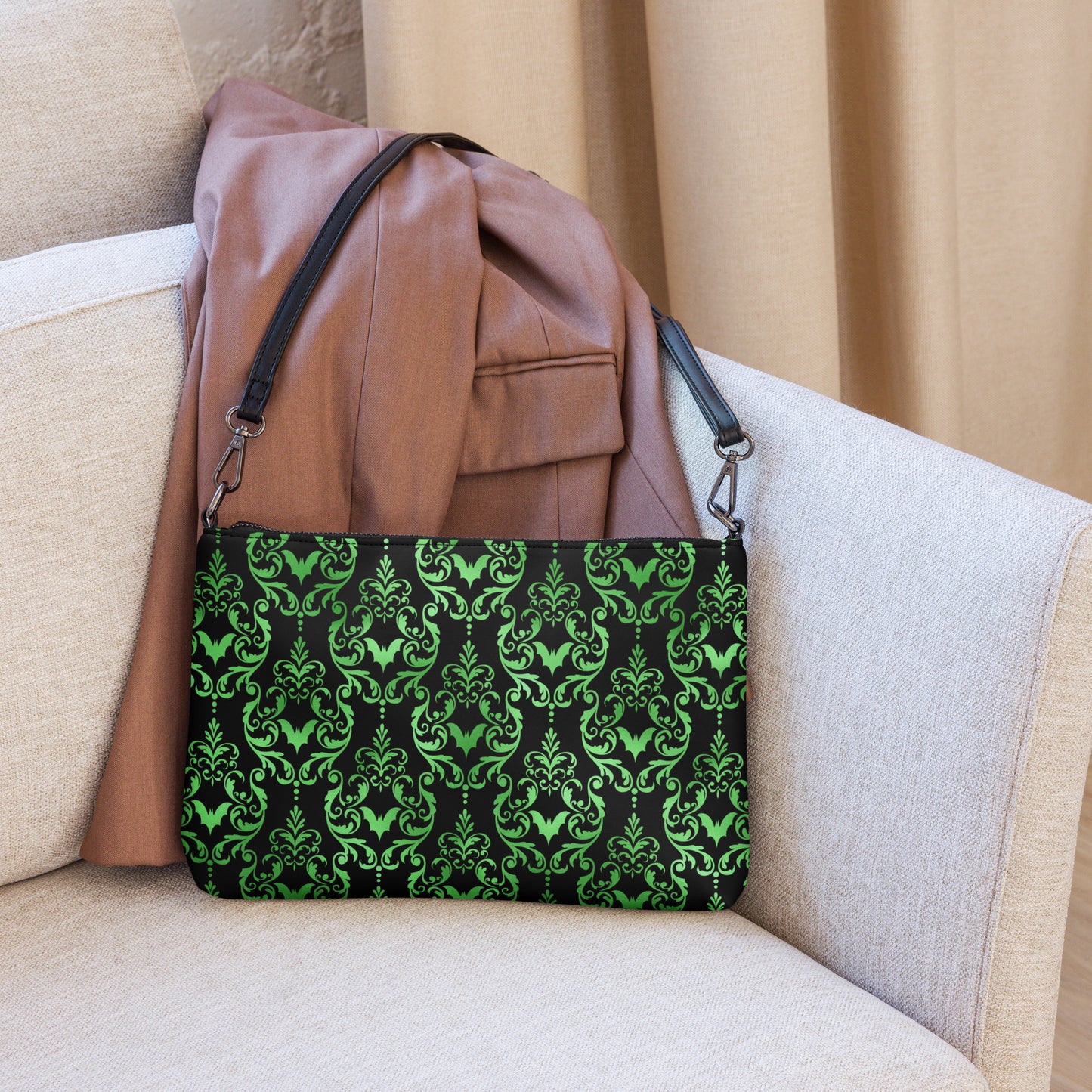 This black crossbody shoulder bag converts into a large wristlet clutch features a retro wallpaper print of green bats and swirls.