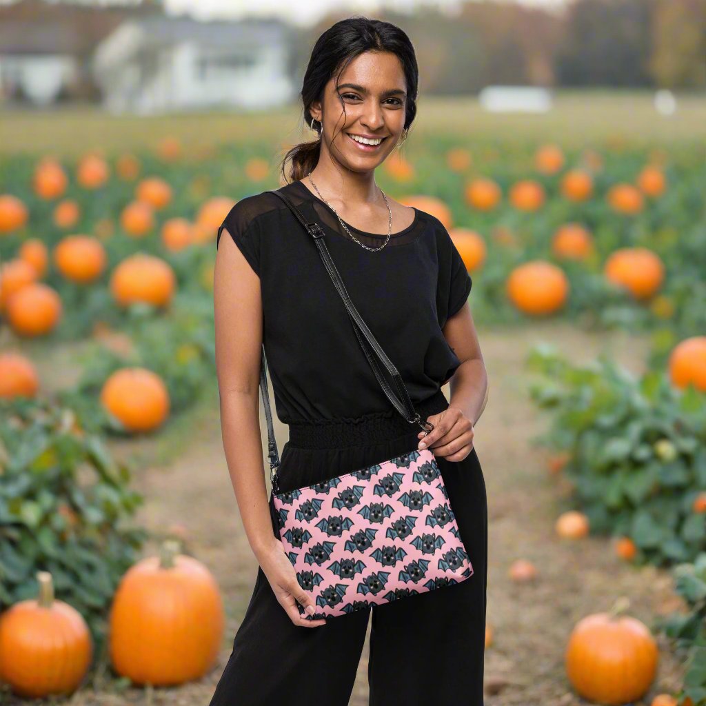 This crossbody shoulder purse converts into a large wristlet clutch. It features adorable grey bats with a pink background.