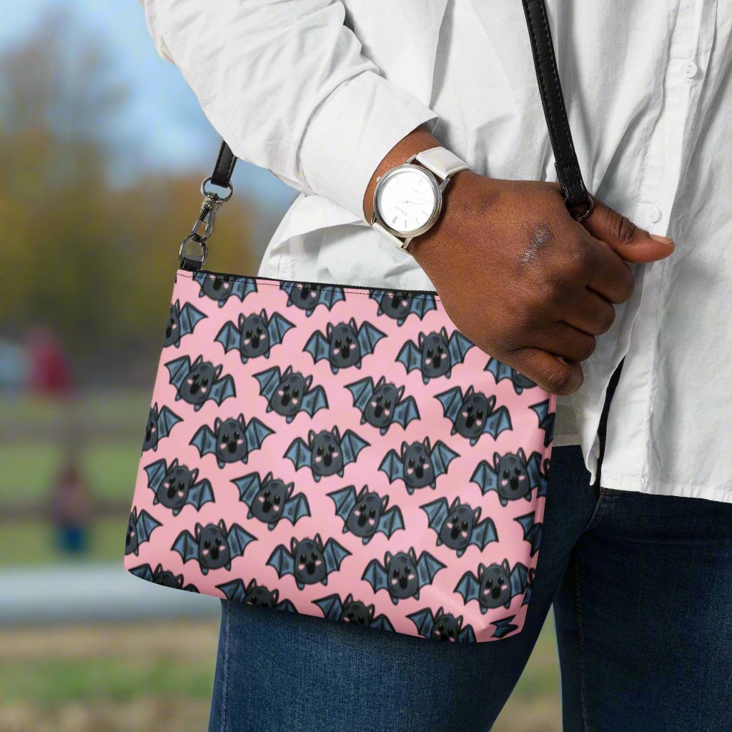 This crossbody shoulder purse converts into a large wristlet clutch. It features adorable grey bats with a pink background.