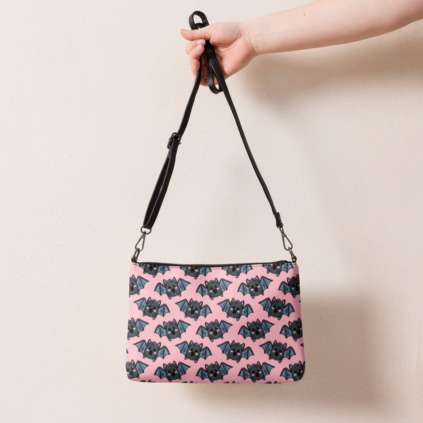 This crossbody shoulder purse converts into a large wristlet clutch. It features adorable grey bats with a pink background.