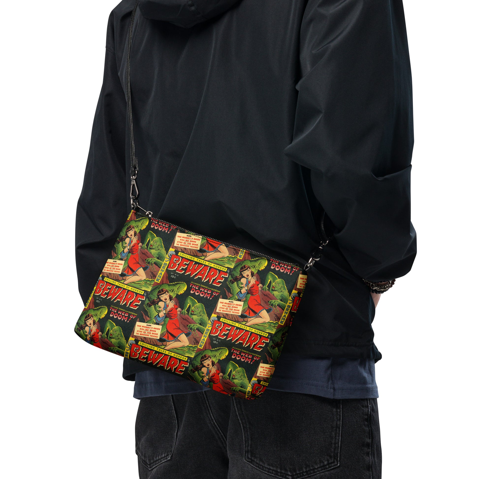 This crossbody bag comesfeatures the print of a retro comic that is Beware the Web of Doom with a gothic noir print of green creatures and a scared woman in red. This is printed in a staggered pattern.