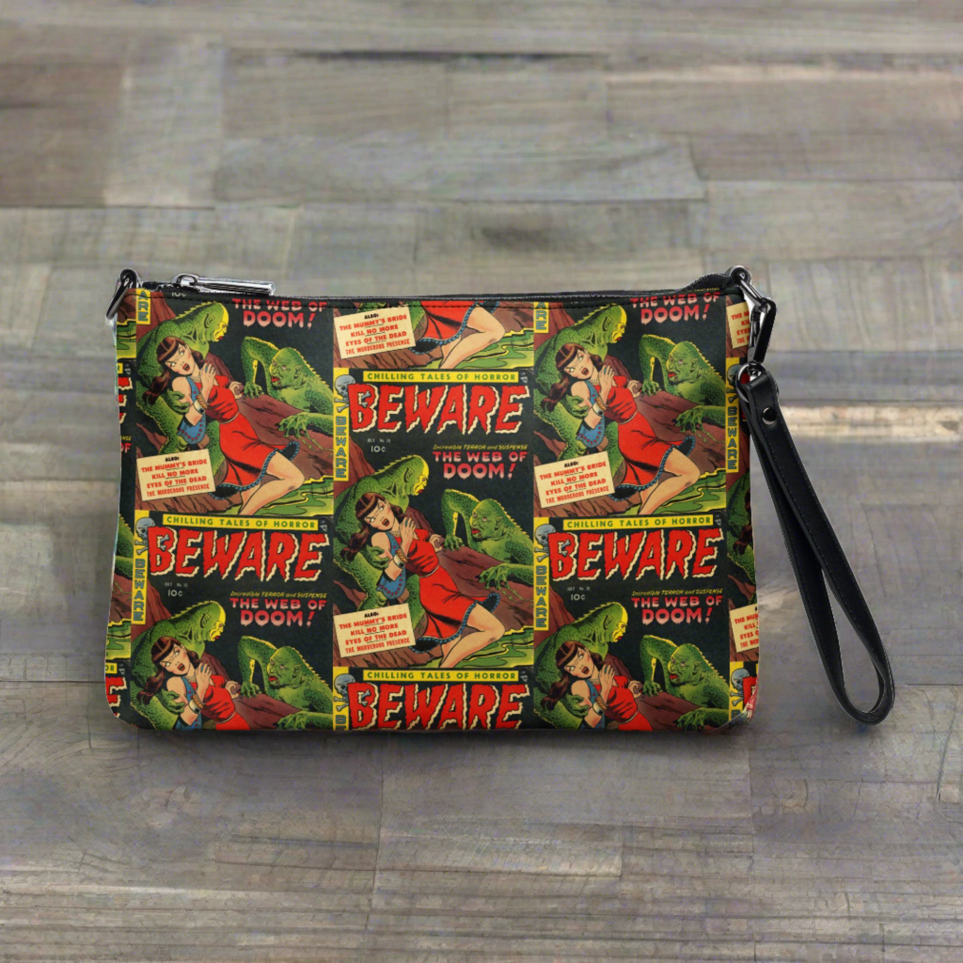 This crossbody bag comes with a wristlet option and is featured in this photo. The print is a retro comic that is Beware the Web of Doom with a gothic noir print of green creatures and a scared woman in red. This is printed in a staggered pattern.