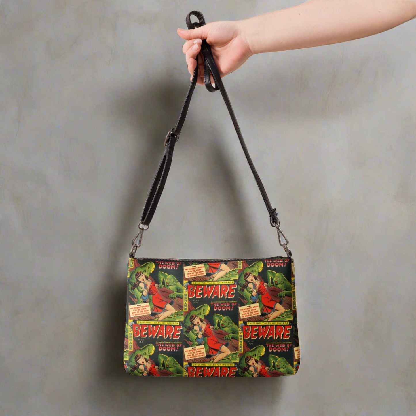 This crossbody bag comesfeatures the print of a retro comic that is Beware the Web of Doom with a gothic noir print of green creatures and a scared woman in red. This is printed in a staggered pattern.