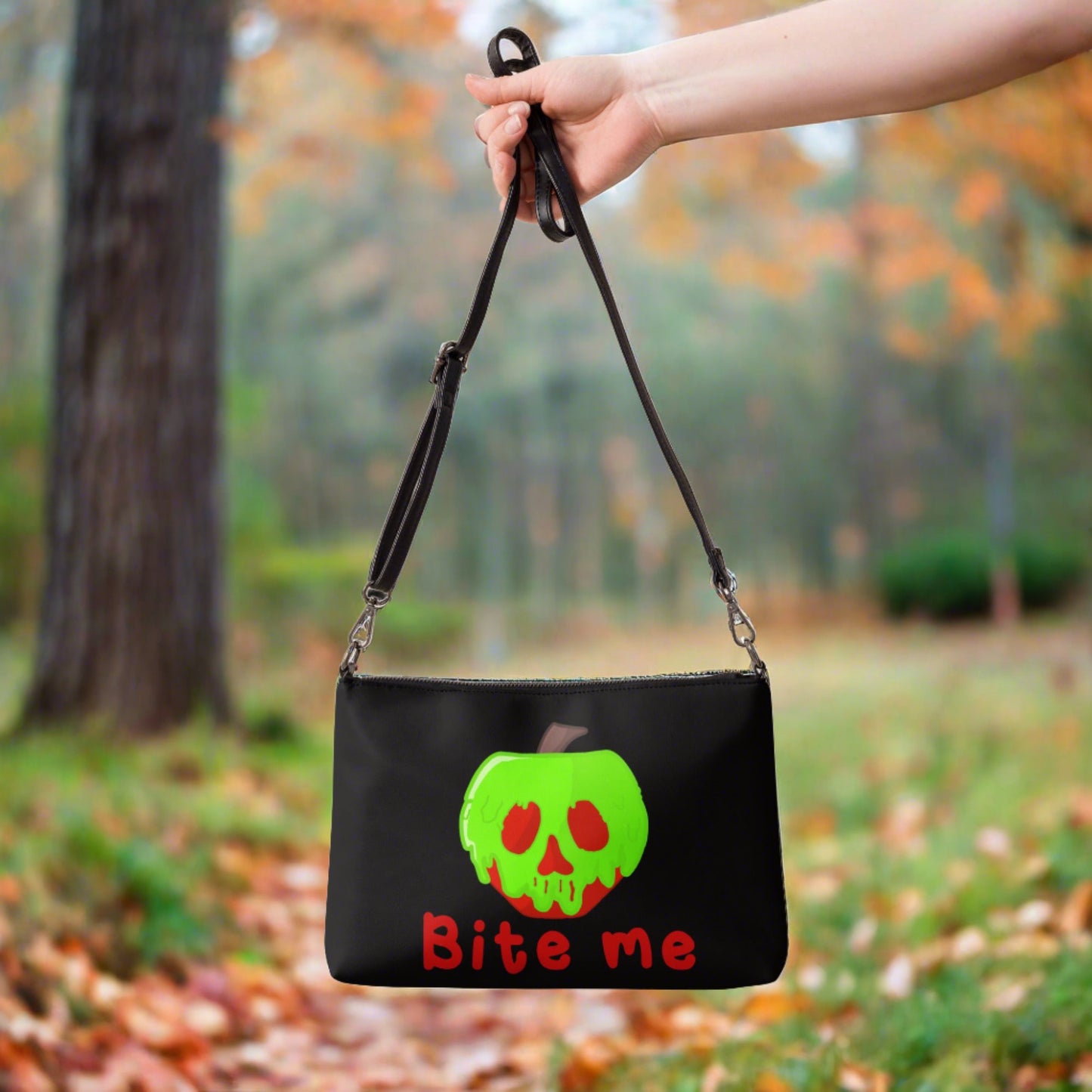 This black crossbody purse features a large red apple dipped in green poison with the words Bite Me underneath and the back is a small size in a patterned print.