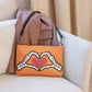 This orange crossbody purse converts to a large wristlet clutch. It features a distressed print of skeleton hands forming a heart with a red heart inside. One side the design is large and the other is a smaller patterned print.