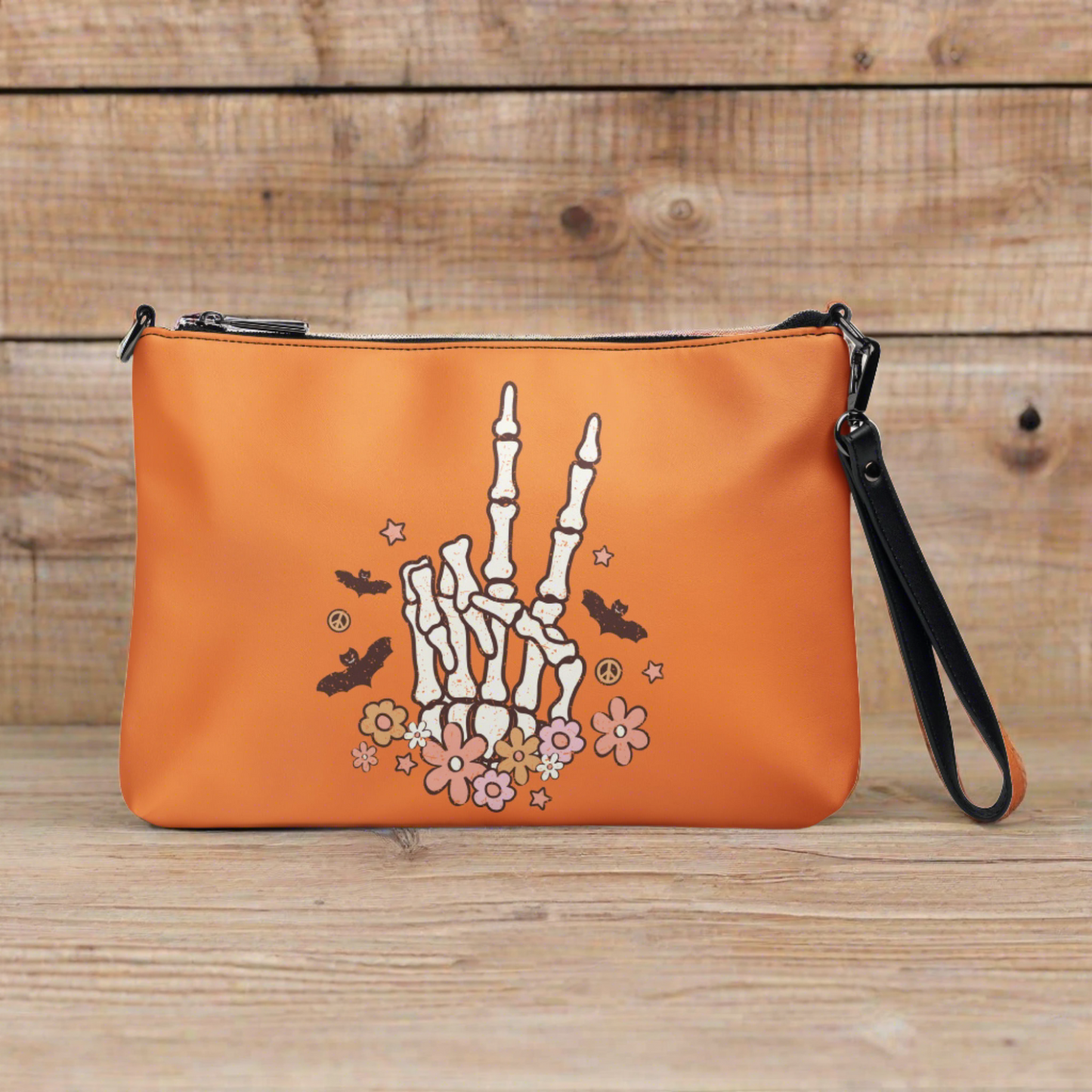 This orange crossbody purse features a skeleton hand making a peace sign surrounded by bats, flowers and peace signs.