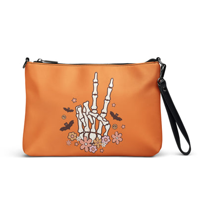 This orange crossbody purse features a skeleton hand making a peace sign surrounded by bats, flowers and peace signs.