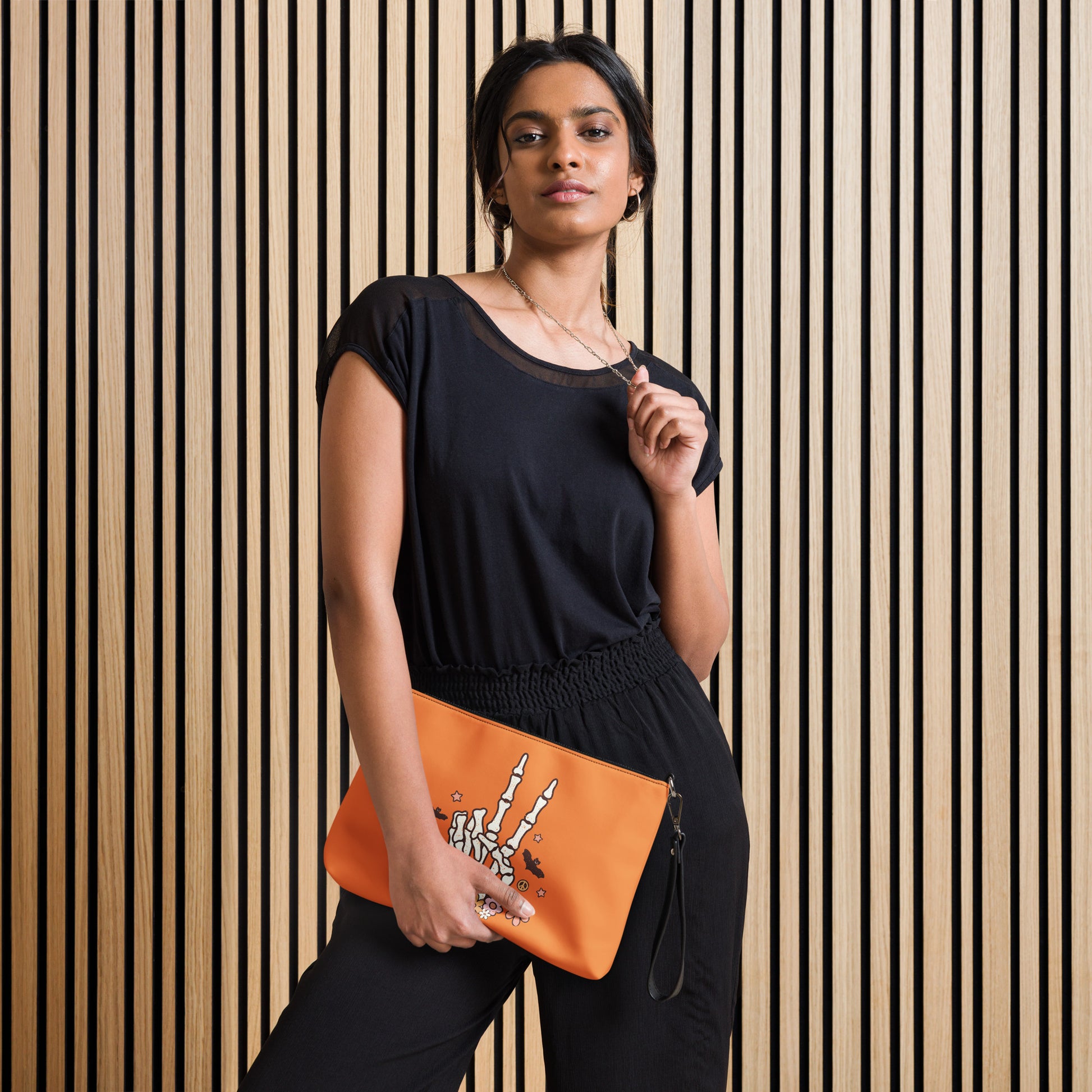 This orange crossbody purse features a skeleton hand making a peace sign surrounded by bats, flowers and peace signs.