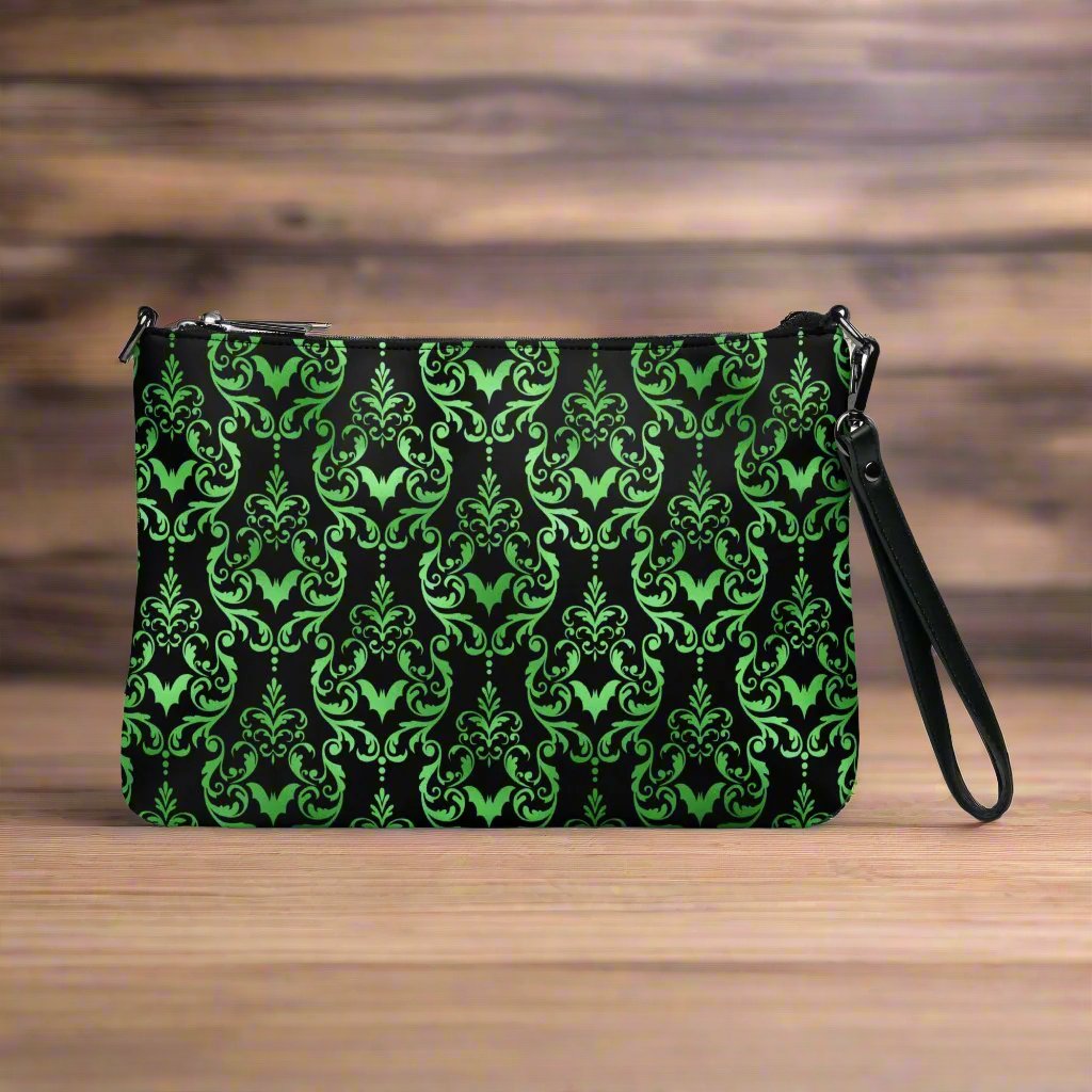 This black crossbody shoulder bag converts into a large wristlet clutch features a retro wallpaper print of green bats and swirls.