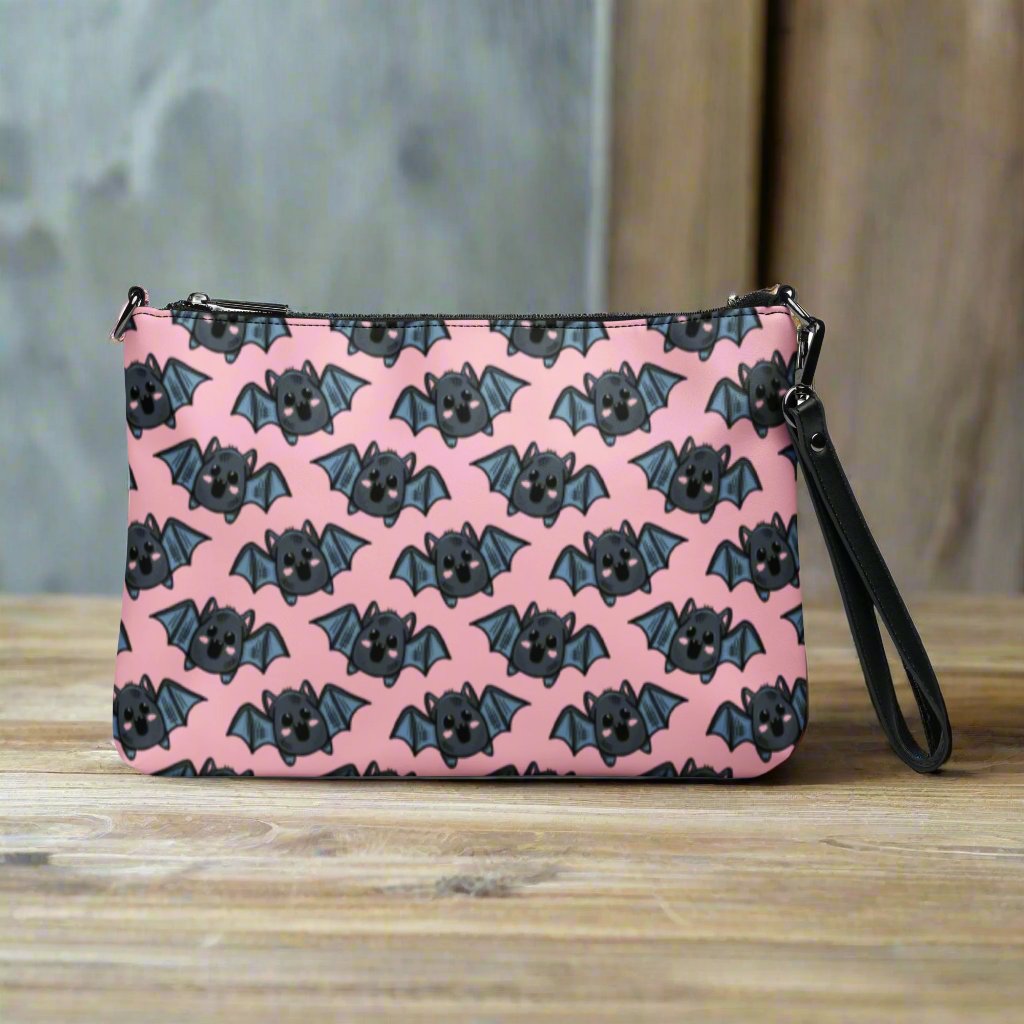 This crossbody shoulder purse converts into a large wristlet clutch. It features adorable grey bats with a pink background.