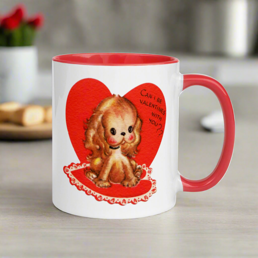 This ceramic glossy coffee cup features a vintage midcentury Valentine's Day illustration of a golden puppy sitting on a heart rug. There is a heart behind her that says Can I be Valentines with you?