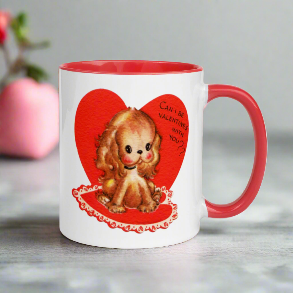 This ceramic glossy coffee cup features a vintage midcentury Valentine's Day illustration of a golden puppy sitting on a heart rug. There is a heart behind her that says Can I be Valentines with you?