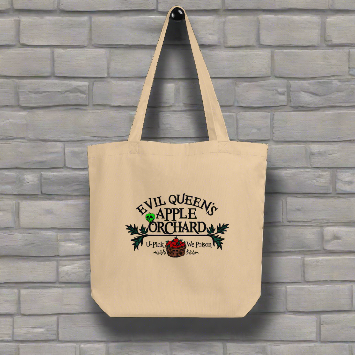 This tote bag says Evil Queen's Apple Orchard U-Pick We Poison and there is a basket of red apples with a poisoned green apple on the O in Orchard.