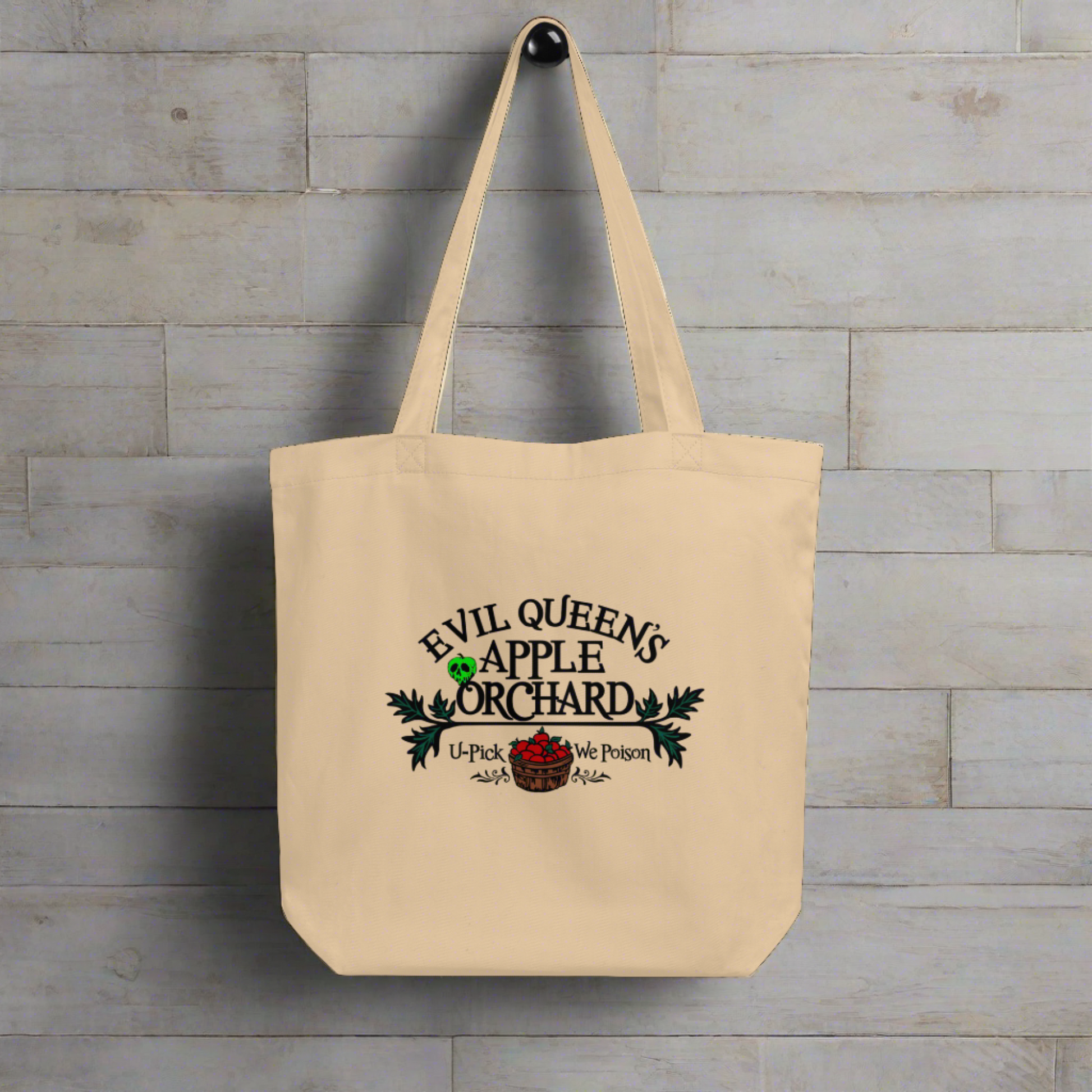 This tote bag says Evil Queen's Apple Orchard U-Pick We Poison and there is a basket of red apples with a poisoned green apple on the O in Orchard.