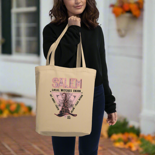 This large cotton eco tote features a Halloween design in pink and black that says Salem Local Witches Union. Sky Above Earth Below Peace Within. Est 1692. There is a pink triangle pointing downward and a pointy witch's hat.