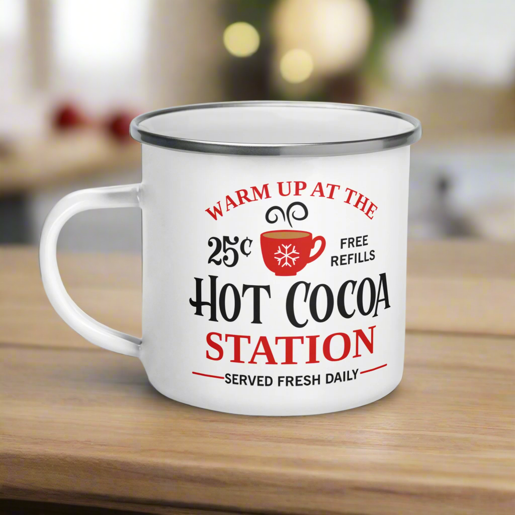 This hot chocolate camping enamel mug features a cute design that says Warm Up At The Hot Cocoa Station Served Fresh Daily.