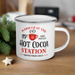 This hot chocolate camping enamel mug features a cute design that says Warm Up At The Hot Cocoa Station Served Fresh Daily.