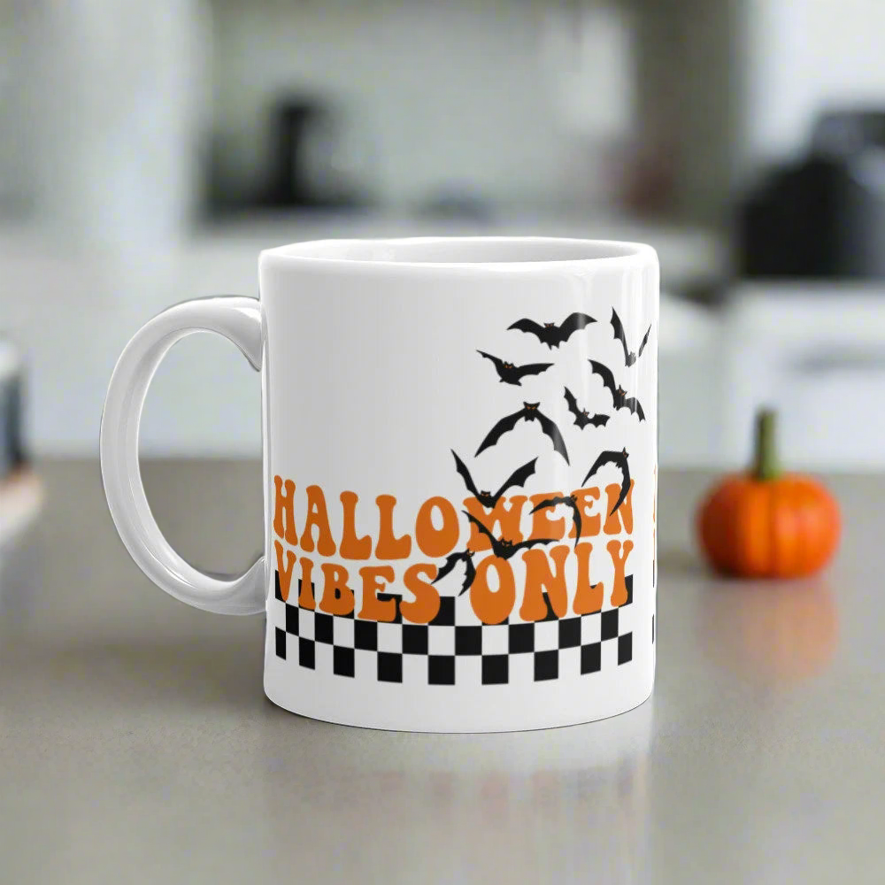 This ceramic glossy Halloween mug features a retro style print that says Halloween Vibes Only. There are flying bats and a black and white checkered print at the bottom.