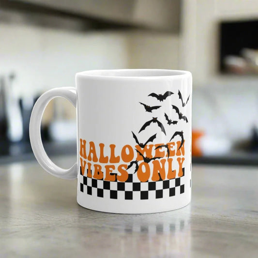 This ceramic glossy Halloween mug features a retro style print that says Halloween Vibes Only. There are flying bats and a black and white checkered print at the bottom.