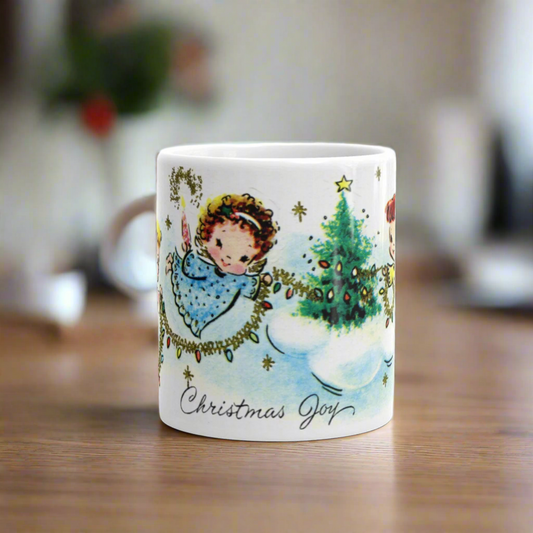 This ceramic glossy coffee mug features a midcentury Christmas illustration that says Christmas Joy and features three young angels flying and decorating a Christmas tree with tinsel and lights. There is a blond, brunette, and redhead angel.