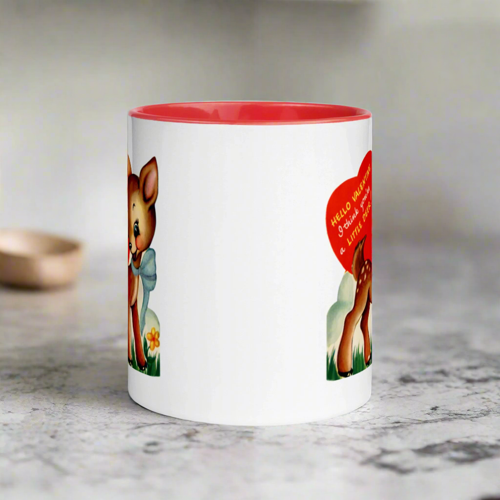 This ceramic glossy coffee mug features a retro midcentury Valentine's Day illustration of a young deer wearing a blue bow around her neck. There is a red heart that says Hello Valentine I think you're a little deer!