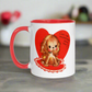 This ceramic glossy coffee cup features a vintage midcentury Valentine's Day illustration of a golden puppy sitting on a heart rug. There is a heart behind her that says Can I be Valentines with you?