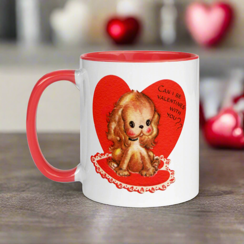 This ceramic glossy coffee cup features a vintage midcentury Valentine's Day illustration of a golden puppy sitting on a heart rug. There is a heart behind her that says Can I be Valentines with you?