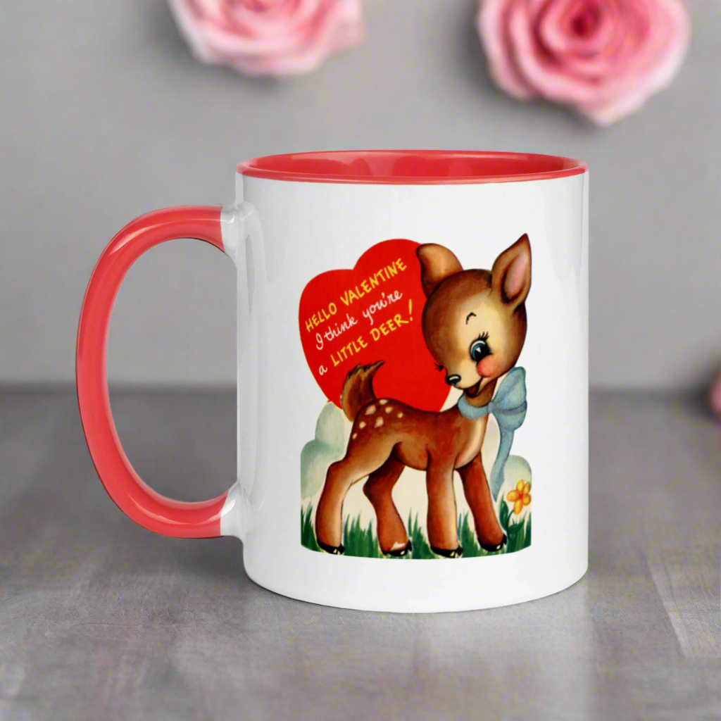 This ceramic glossy coffee mug features a retro midcentury Valentine's Day illustration of a young deer wearing a blue bow around her neck. There is a red heart that says Hello Valentine I think you're a little deer!