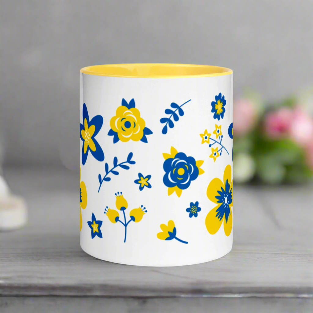 This ceramic glossy mug has a yellow handle and interior. The artwork features blue and yellow Ukranian country flowers.