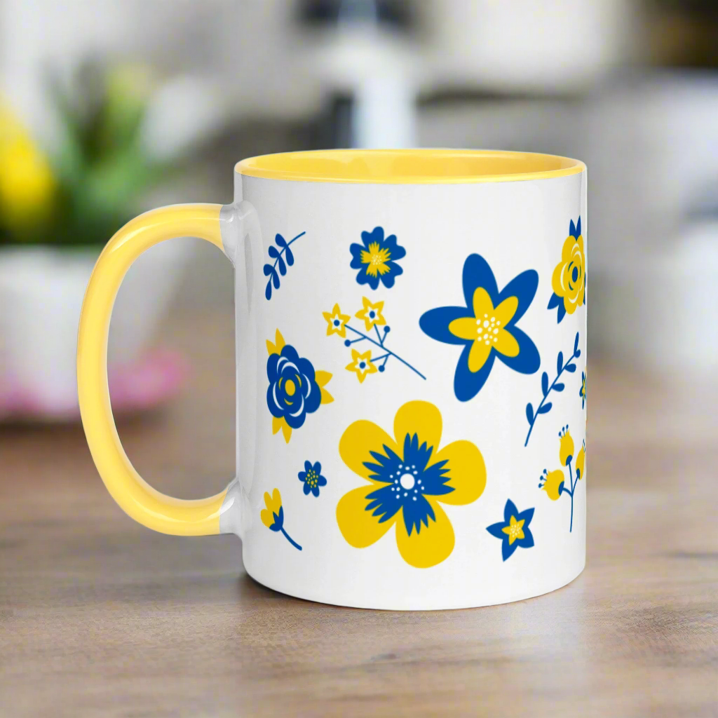 This ceramic glossy mug has a yellow handle and interior. The artwork features blue and yellow Ukranian country flowers.