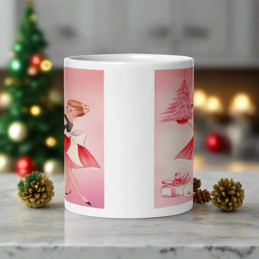 This glossy ceramic coffee mug features a midcentury retro Christmas illustration of a woman dressed in black and pink holding a small pink Christmas and ornament. There are a couple of presents and a pink background.