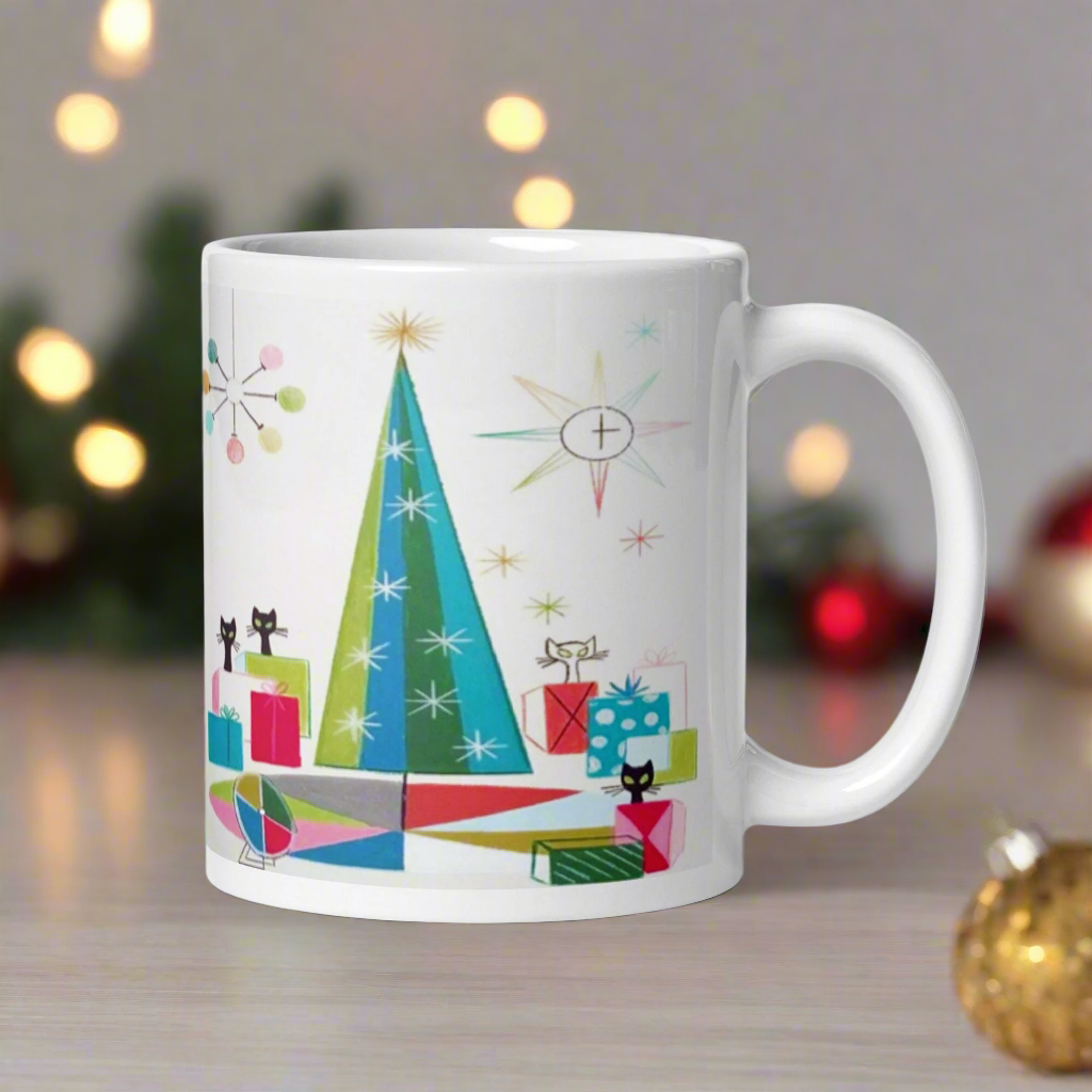 This ceramic glossy Christmas coffee mug features an atomic Midcentury illustration of cats peeking out from behind presents around a Christmas tree. There is a colorful round rug, light projector, clock and chandelier all in atomic era style.