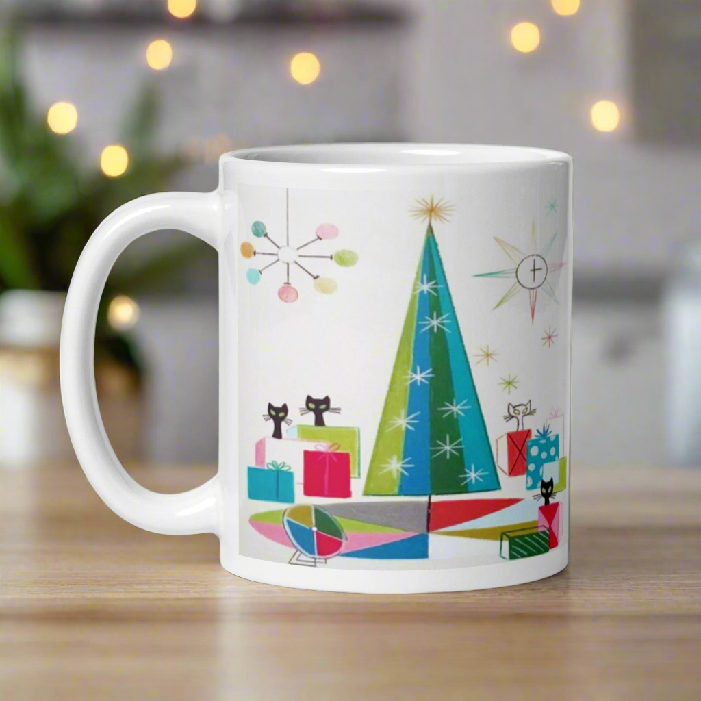 This ceramic glossy Christmas coffee mug features an atomic Midcentury illustration of cats peeking out from behind presents around a Christmas tree. There is a colorful round rug, light projector, clock and chandelier all in atomic era style.