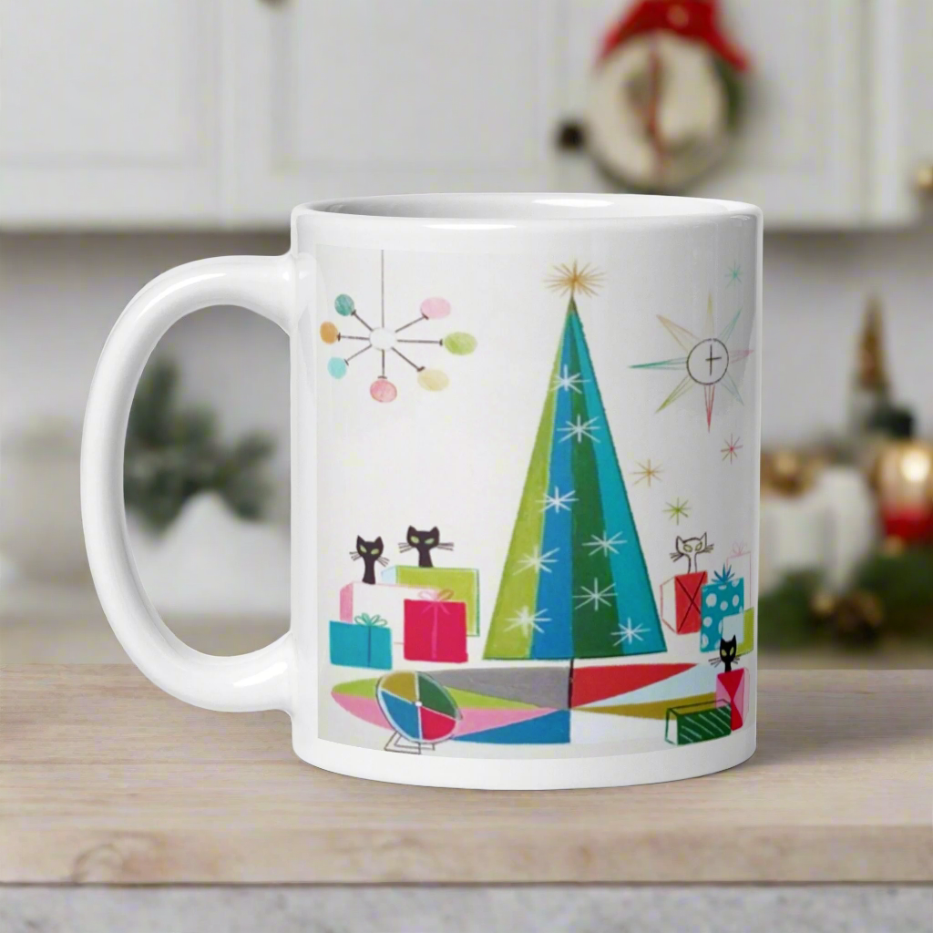 This ceramic glossy Christmas coffee mug features an atomic Midcentury illustration of cats peeking out from behind presents around a Christmas tree. There is a colorful round rug, light projector, clock and chandelier all in atomic era style.