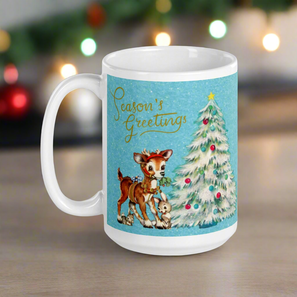 This glossy ceramic coffee mug features 
 Midcentury vintage artwork of an adorable reindeer with holly in her mouth, bunnies, and a Christmas Tree. There is gold lettering that says Season's Greetings and a blue felt background.